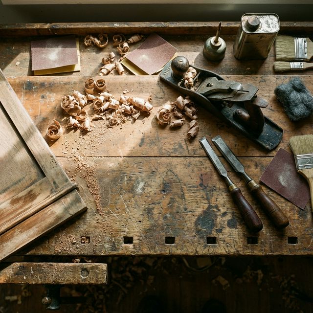 A well-worn workbench with hand planes, chisels, and wood shavings.